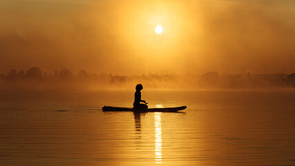 Naklejka na ściany i meble Man sitting on sup board and enjoying beautiful sunrise