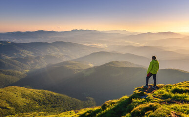 Sporty man on the mountain peak looking on mountain valley with sunbeams at colorful sunset in...
