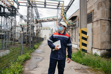 An electrical substation engineer inspects modern high-voltage equipment in a mask at the time of pondemia. Energy. Industry