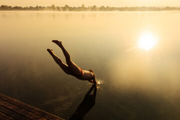 Fototapeta na wymiar Muscular sportsman plunging into lake from wooden pier