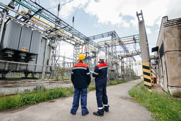 Two specialist electrical substation engineers inspect modern high-voltage equipment. Energy....
