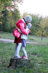 two sisters stand on a tree stump, hug and kiss