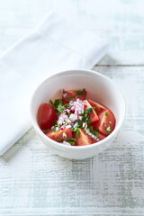 Simple salad with cherry tomatoes, red onion and fresh herbs. Bright wooden background. Close up.	