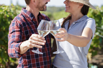 couple with wineglasses embracing while sitting at vineyard