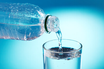 pouring fresh bottled water to glass over blue background. copy space. water flow. energy symbol conceptual