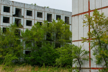 Fototapeta premium An abandoned multi-storey building stands in the middle of a green field. Multi-storey building without windows