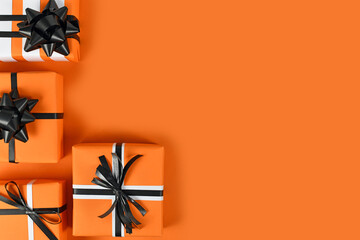Gift boxes with traditional Halloween colors on left side of  orange background with empty copy...