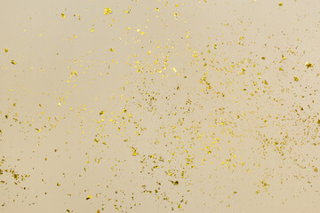 Golden confetti on beige paper trendy background. Festive holiday backdrop. Birthday congratulations Christmas New Year. Flat lay, top view, copy space.