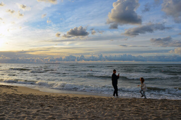 Big brother and little sister on the background of the Baltic sea run away from the waves and fool around on camera.