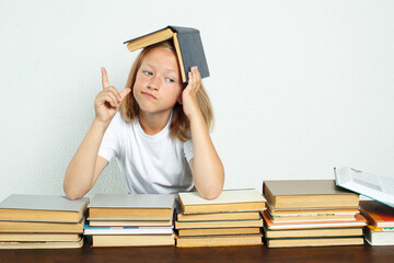The student sits at the table, with a textbook on her head. She raised her finger emotionally. Books are spread out nearby