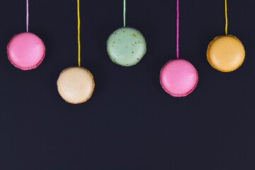 Colorful French macaron attached to strings hanging from top of black background with empty copy...