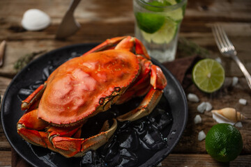 King crab on black round plate with ice cube. The glass with mojito, lime, seashells and mint are...