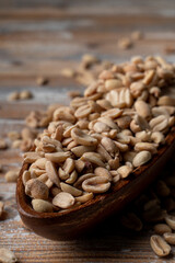 A big pile of crunchy salted peanut in a wooden bowl, close up view on wooden background