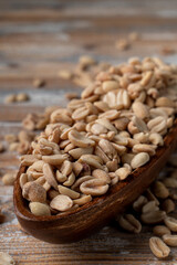 A big pile of crunchy salted peanut in a wooden bowl, close up view on wooden background