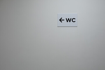 White plastered wall with WC sign and arrow pointer. Empty clean wall with a pointing sign indicating the location of the hygienic room, toilet WC