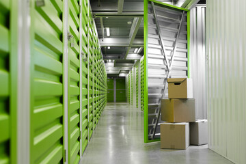Background image of green self storage facility with opened unit door and cardboard boxes, copy...