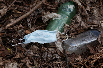 Fototapeta premium Environmental pollution with new types of waste resulting from the epidemic of coronavirus Covid-19. Used surgical face masks and plastic bottles are thrown to the ground