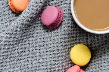 Background with gray plaid, coffee, cappuccino and multicolored appetizing macaroons, top view, flat lay. home comfort, warmth, care, tenderness.