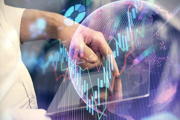 Double exposure of man's hands holding and using a digital device and forex graph drawing. Financial market concept.