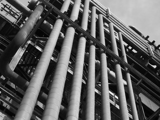 Black and white view of old rusty industrial pipe covered oil and petrochemical refinery tower.  