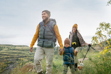 Three happy backpackers in warm casualwear and their cute pet enjoying trip