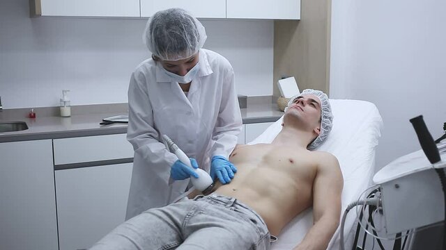Confident female beautician performing body ultrasound cavitation procedure for young man at aesthetic clinic