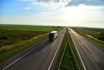 Truck with semi-trailer driving along highway on the sunset background. Goods delivery by roads. Services and Transport logistics. soft focus. Object in motion.