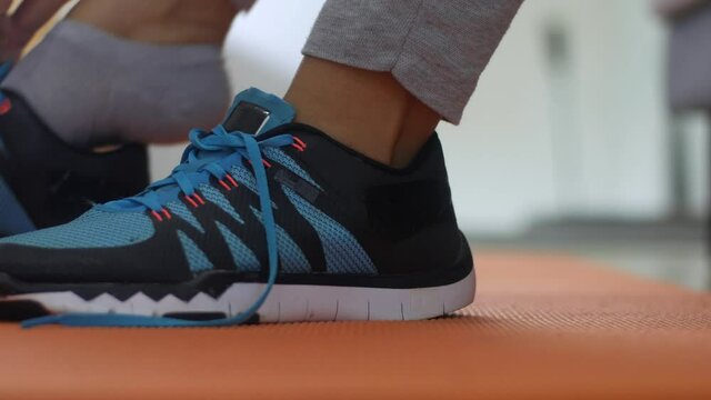 Young woman tying her shoelaces in her bedroom, preparing for workout, indoor home exercise concept, close up image