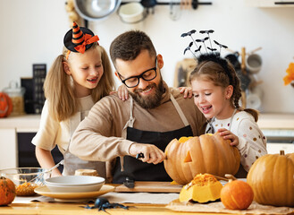 happy family   father and children prepare for Halloween by carving pumpkins at home in kitchen.