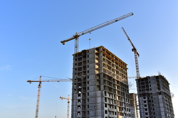 Tower cranes in action on blue sky background. Construction of new multi-storey buildings. Residential building is being constructed use of crane. Pouring of concrete in formwork