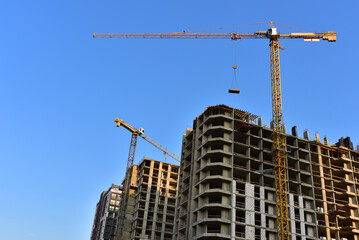 Fototapeta premium Tower cranes in action on blue sky background. Construction of new multi-storey buildings. Residential building is being constructed use of crane. Pouring of concrete in formwork