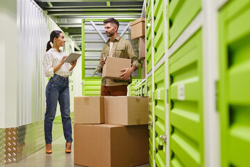 Full length portrait of modern couple using digital tablet while loading boxes into self storage...