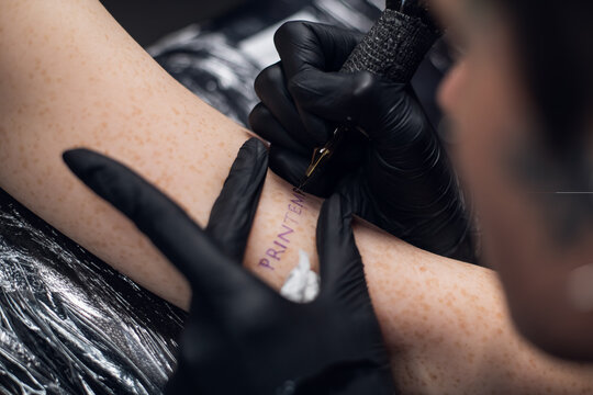The process of tattooing on a woman's hand inscriptions in French printemps -- spring. Close-up in a tattoo parlor