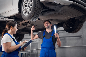 Workman and mechanic inspect the bottom of the car with a flashlight