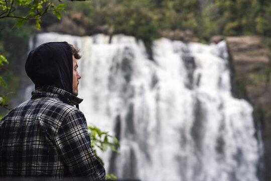 Young man wearing hoodie and admiring the nature in waterfall landscape. Inspirational concept