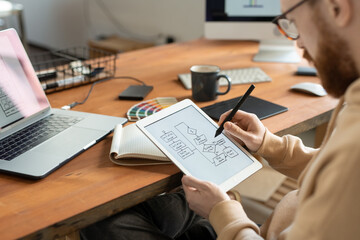 Young bearded freelance programmer holding stylus over touchscreen