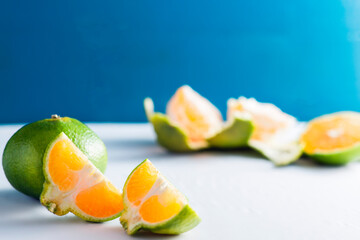 Peeled and sliced green mandarins over white backdrop near wooden blue vintage wall with copy...