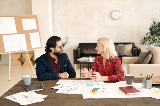 Young bearded designer and his happy matue blond female colleague talking