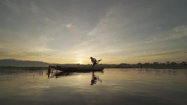 Slow motion of Silhouette Fisherman casting or throwing a net for catching freshwater fish in nature lake or river with reflection in morning time in Asia in Thailand. People.