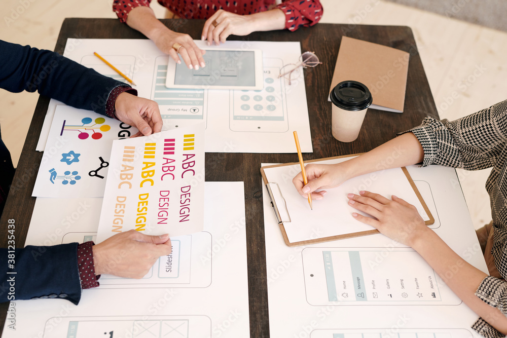 Poster Hands of three creative mobile application developers working by wooden table