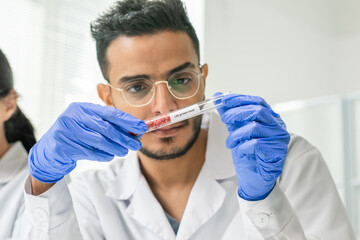 Gloved male worker of food quality control looking at tiny pieces of raw meat