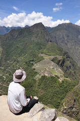 Fototapeta na wymiar A hiker sit son a ledge on Huayna (Wayna) Picchu and looks across at Machu Picchu