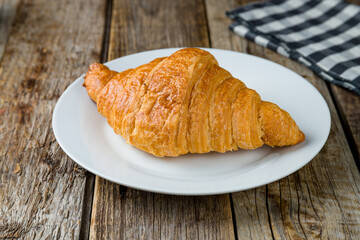 The classic croissant on a white plate on old wooden table