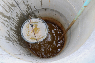 pulling out bucket full of drink water from the well, view of the water well, scooping water with buckets from water well, Sump
