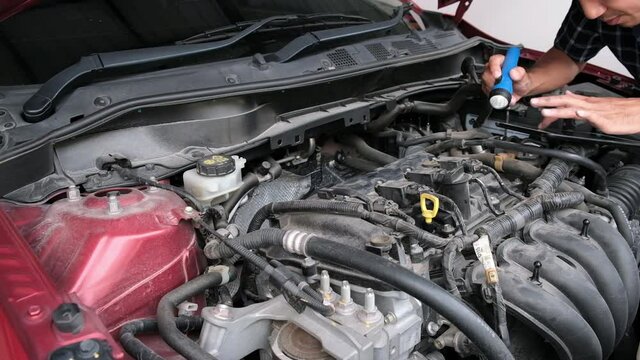 Asian Man mechanic inspection Shine a torch car engine checking bug in engine from application smartphone.Red car for service maintenance insurance with car engine.for transport automobile automotive