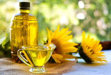 sunflower oil poured into glass saucepan is on a canvas napkin. near a bottle of oil and flowers....