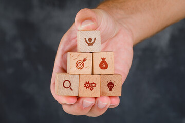 Business concept on grungy grey background side view. hand holding wooden blocks with icons.