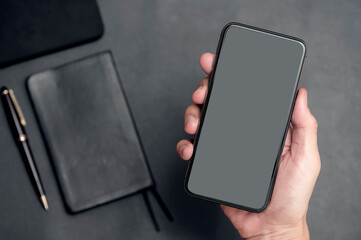  Closeup man hand holding black smartphone with blank screen  on black background.