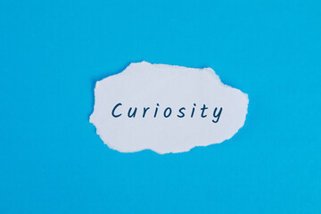 Business concept with curiosity word on torn paper on blue background flat lay.
