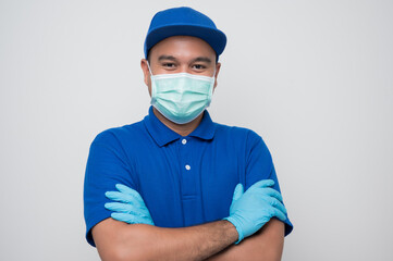 Blue delivery asian man wearing protection mask and medical rubber gloves standing with arm crossed on isolated white background safety deliver concept..